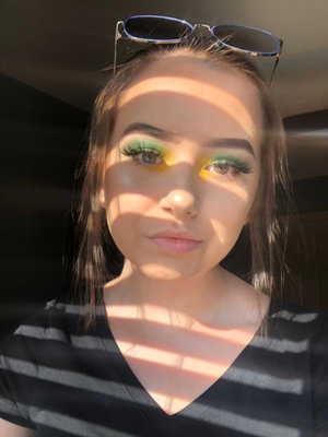 Woman with colorful eye makeup and sunglasses on head, wearing striped top, indoor selfie.