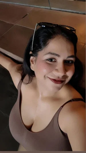 Woman with dark hair wearing brown tank top, smiling in indoor setting.