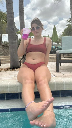 Woman in red bikini sitting poolside holding drink.