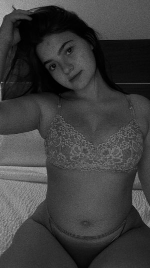Woman in lace bra and thong lying on bed, dark hair, indoor setting.