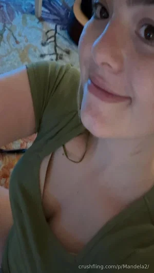 Woman in olive green top, smiling, close-up selfie in indoor setting.