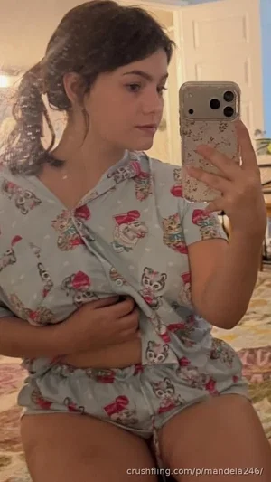 Woman in cat-print pajamas taking mirror selfie in bedroom.