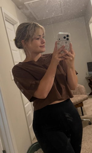 Blonde woman taking mirror selfie in brown top and black leggings.