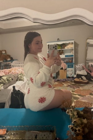 Woman with wet brunette hair in white fluffy outfit, bedroom mirror selfie.