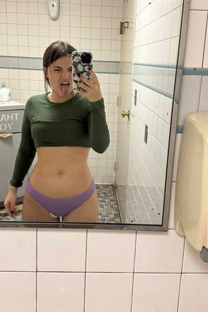 Woman in green crop top and purple thong in bathroom mirror selfie.