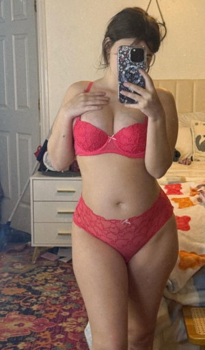 Curvy woman in red lace lingerie taking mirror selfie in bedroom.