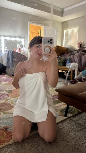 Woman in towel taking selfie in bedroom.