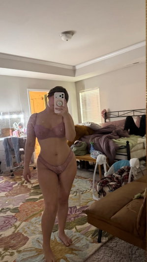 Woman in pink lingerie taking mirror selfie in bedroom.