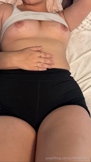Woman with curvy body wearing white top and black shorts lying on bed.