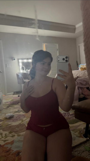 Curvy woman in red lingerie taking mirror selfie in bedroom.