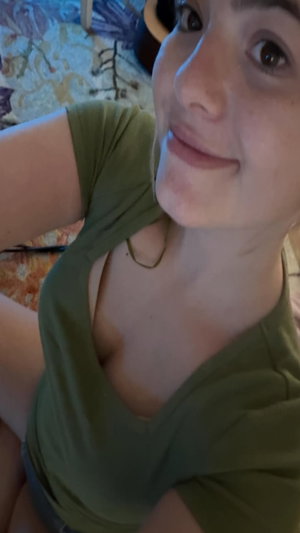 Woman in olive green top, smiling, indoor setting, close-up selfie.