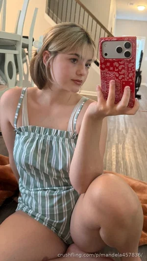 Woman in striped romper taking mirror selfie indoors, sitting on floor.