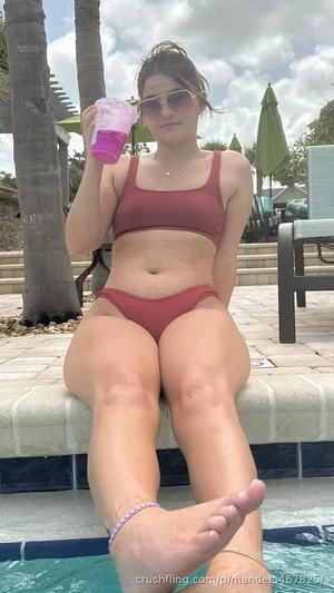 Woman in red bikini sitting by pool, holding pink drink, wearing sunglasses.