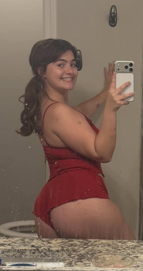Smiling woman in red dress taking wet mirror selfie in bathroom.