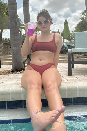 Woman in red bikini sits poolside holding drink.