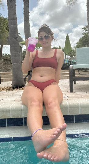 Woman in red bikini sitting poolside holding drink.