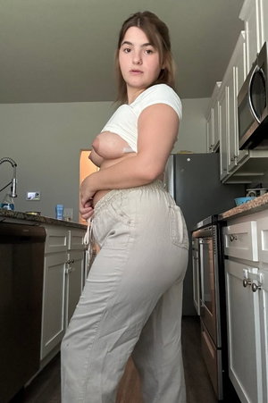 Woman in white top and beige pants standing in kitchen.