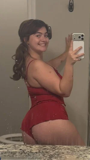Woman in red dress taking mirror selfie in bathroom, curvy body type.