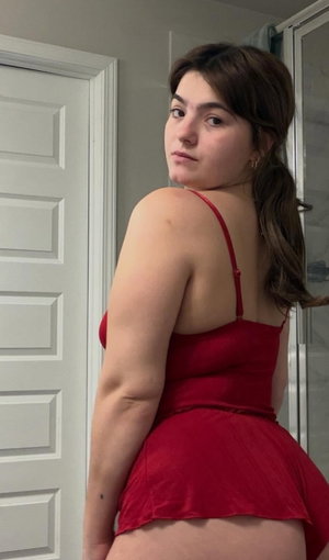 Curvy brunette in red dress posing in bathroom.