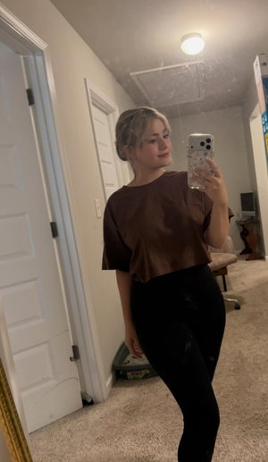 Woman in brown top and black leggings taking mirror selfie indoors.