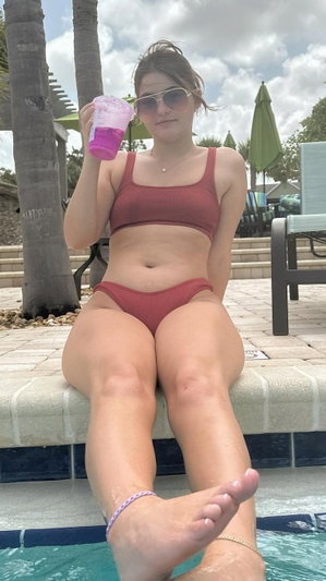 Woman in red bikini sits poolside holding drink.