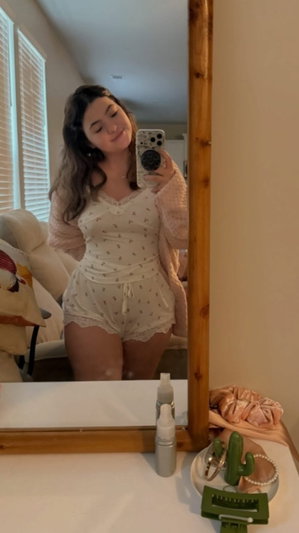 Woman in white lace romper taking mirror selfie indoors.