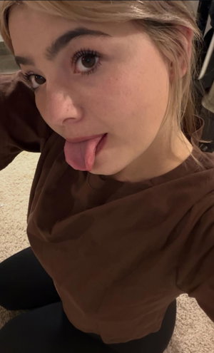 Blonde woman in brown top taking indoor selfie.
