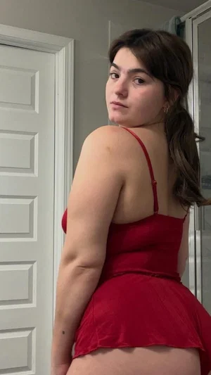 Woman in red dress posing indoors, back to camera, showing shoulders and hips.