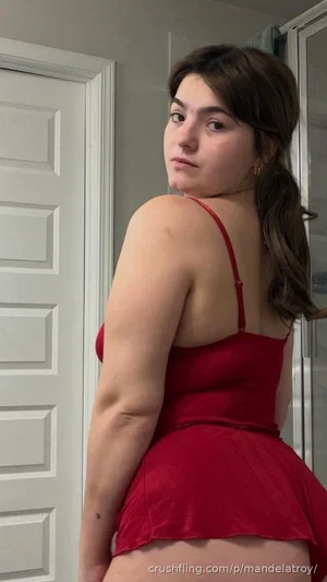 Woman in red spaghetti strap dress, standing indoors, facing away but turning head toward camera.