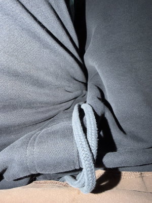 Close-up of gray hoodie tied at waist over beige pants, indoor setting.