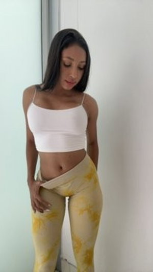 Woman in white crop top and yellow patterned leggings standing indoors.