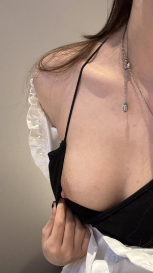 Woman with long brown hair wearing black top and necklace indoors.