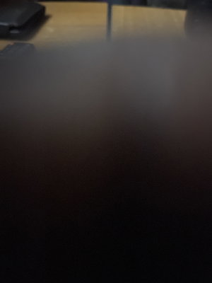 Blurry dark image with indistinct shapes, possibly a table surface and object.