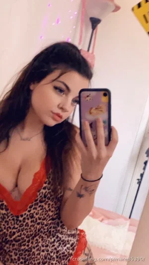 Woman in leopard print lingerie with red trim, taking mirror selfie in bedroom.