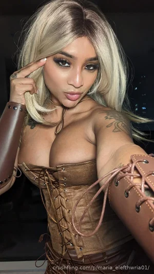 Woman with blonde hair in brown corset and arm sleeves, posing indoors.