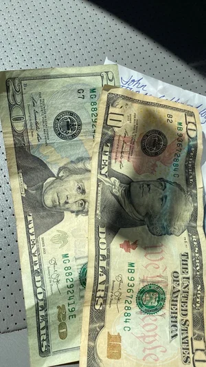 Two US dollar bills, twenty and ten, lying on a perforated surface.