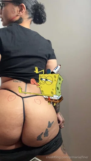 Woman in black top and thong with tattoos, showing backside in indoor setting.