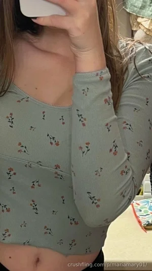 Woman in floral long-sleeve crop top, holding phone, indoor setting.