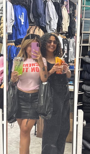 Blonde in pink top black mini skirt, curly-haired in black outfit, store mirror selfie.