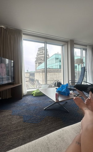 Bare legs with ankle tattoos in hotel room with city view.