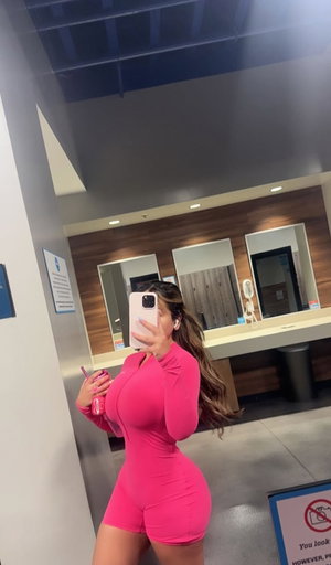 Woman in pink romper taking mirror selfie in bathroom.
