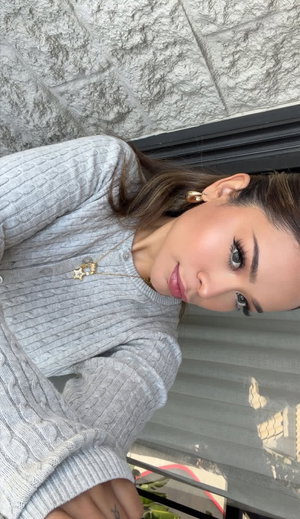 Brunette woman in gray sweater taking indoor selfie.