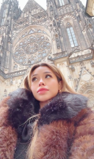 Woman with blonde hair in fur coat before cathedral.