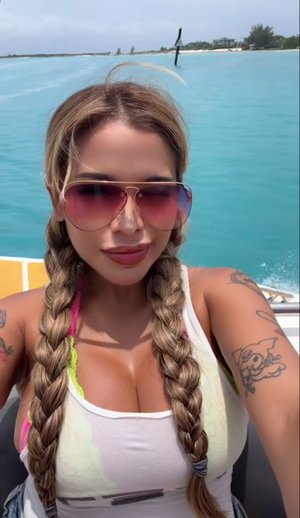 Woman with braided hair and tattoos wearing a white tank top on a boat in blue water.