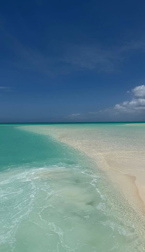 Clear turquoise water meets white sand beach under blue sky.