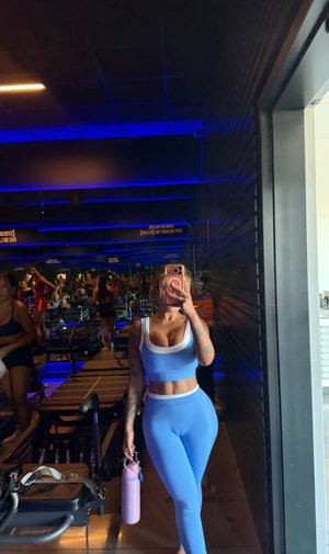 Woman in blue workout outfit taking mirror selfie in gym.