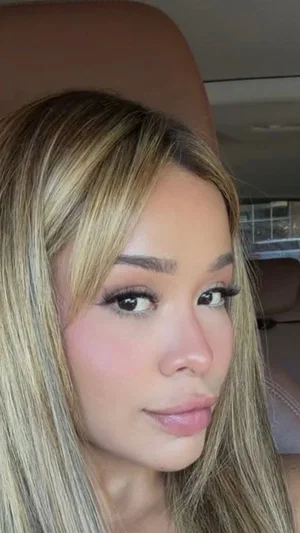 Woman with blonde hair and makeup, taking selfie in car.