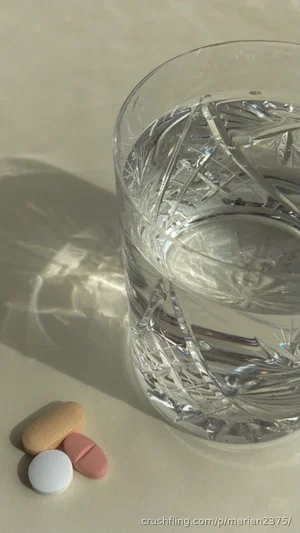 Glass of water with pills on a light surface.