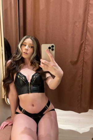 Curvy woman in black lace lingerie takes mirror selfie in fitting room.