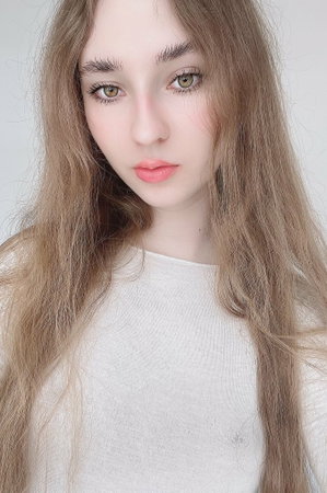 Petite woman with long blonde hair in white top indoors.